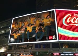 Nighttime Billboard with a Group of Men in Yellow Soccer Jerseys Celebrating, One Holding a Coca-cola Bottle; Text Reads "in 90 Minutes" and Coca-cola Logos Are Visible.