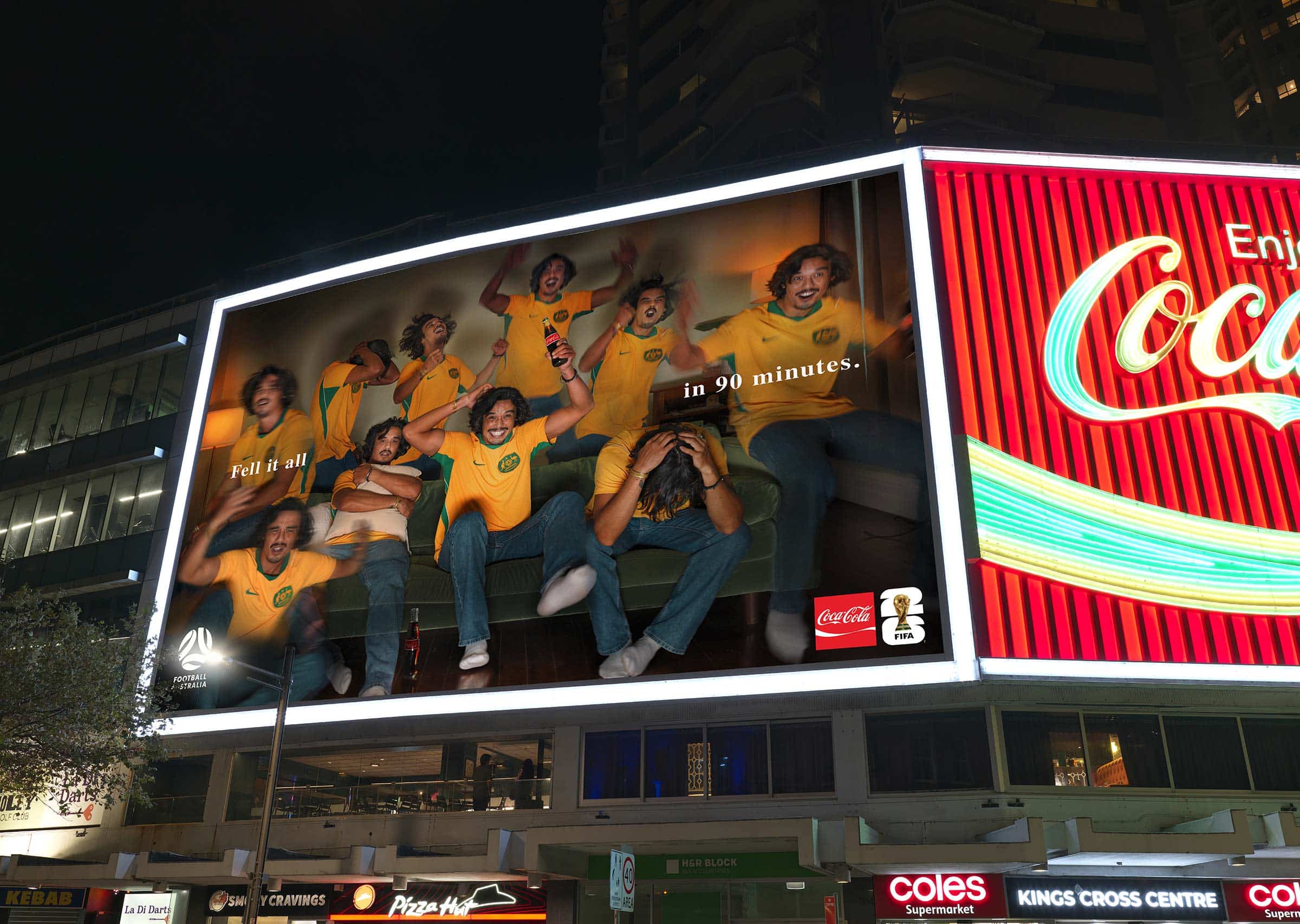 Nighttime billboard with a group of men in yellow soccer jerseys celebrating, one holding a Coca-Cola bottle; text reads