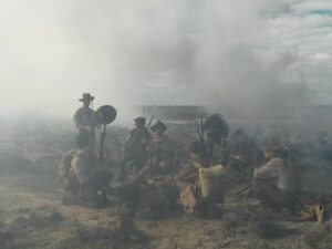 Soldiers in Khaki Uniforms Crouch and Stand with Rifles in a Smoky Desert Battlefield Under a Cloudy Sky.