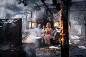Family of Three Sits on a Sofa in a Burned, Smoke-filled Living Room with Flames Nearby.