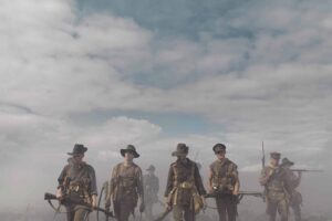 Line of Soldiers in Wwi-era Uniforms Standing with Rifles in a Smoky, Overcast Battlefield.
