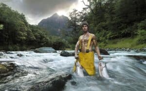 Man Wearing Yellow Waterproof Waders Stands in a Rushing River, Holding Two Fish in Each Hand.