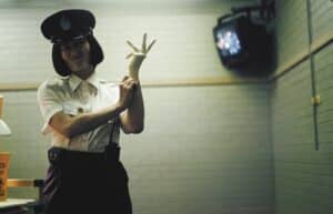 Customs Officer in Uniform and Peaked Cap Making a Peace Sign with a Gloved Hand in a Dim, Indoor Setting.